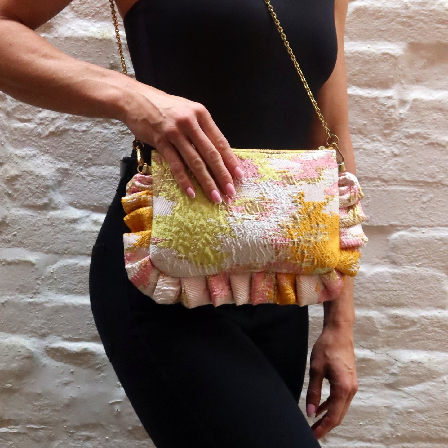 The Dolly Sunset Dreams Frilly Edge Bag is handcrafted in England from vibrant orange, pink, yellow and metallic gold brocade, finished with a yellow zip and elegant gold hardware. Complete with a gold leather wrist strap and bespoke gold chain, it can be worn as a clutch, shoulder or crossbody bag, making it perfect for weddings, festivals, holidays and special occasions.
