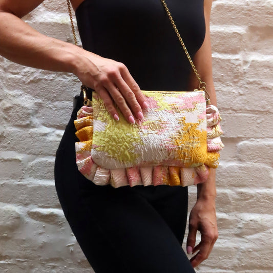 The Dolly Sunset Dreams Frilly Edge Bag is handcrafted in England from vibrant orange, pink, yellow and metallic gold brocade, finished with a yellow zip and elegant gold hardware. Complete with a gold leather wrist strap and bespoke gold chain, it can be worn as a clutch, shoulder or crossbody bag, making it perfect for weddings, festivals, holidays and special occasions.
