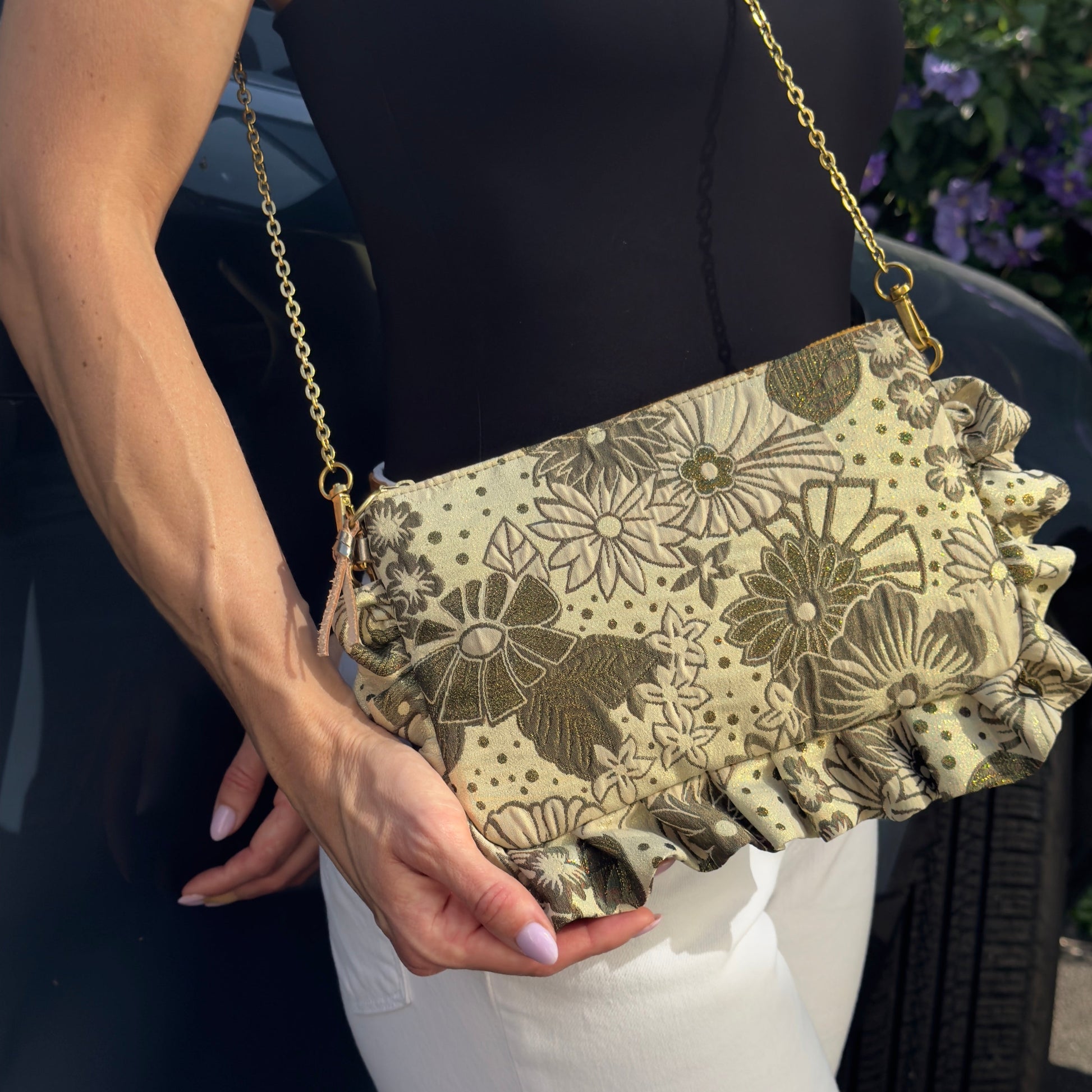 The Psychedelic Flower Power Dolly Frilly Edge Bag is handcrafted in England from luxurious gold, khaki green and cream brocade with a baby pink moiré lining. Wear it as a clutch, shoulder or crossbody bag with the included gold leather wrist strap and bespoke gold chain—perfect for weddings, festivals, holidays and special occasions.
